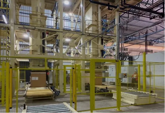 Two-charge lamina press tower with safety fencing and a packed carton on the roller conveyor at a SUR Engenharia reference installation